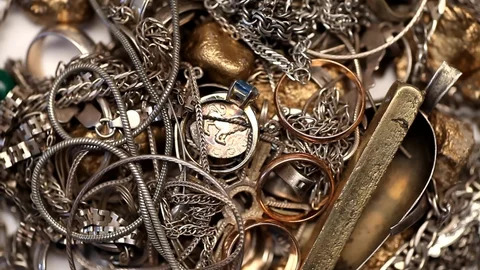 An assorted collection of scrap precious metals, including fragments of gold, silver, platinum, rhodium, and ruthenium jewelry. The pile showcases various pieces, from broken chains and single earrings to damaged rings and old coins. Each piece, despite its current condition, holds potential value and can be transformed into cash at Infinity Coins